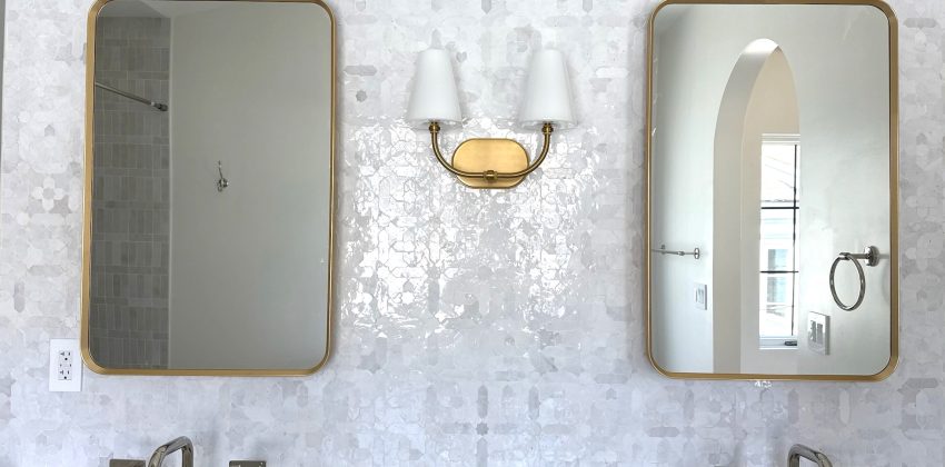 Double vanity bathroom with brass-framed mirrors, brass sconce, and marble backsplash in a Manhattan Beach home remodel