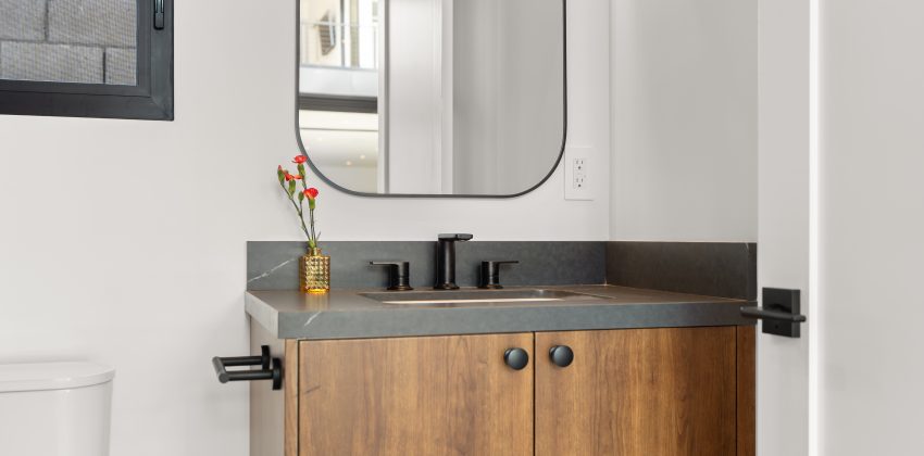 Bathroom vanity with walnut cabinet, concrete-style countertop, matte black fixtures, and arched mirror in Manhattan Beach new home