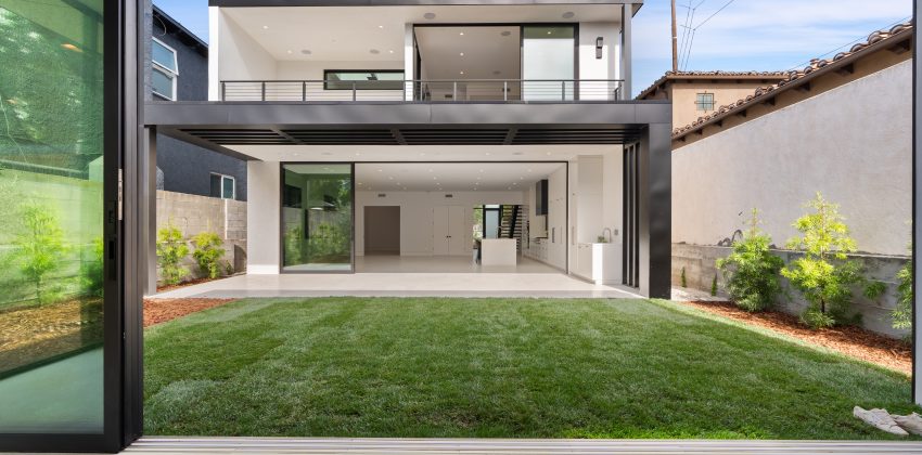 Modern custom home backyard with folding glass doors opening to grass yard and open-concept kitchen in Manhattan Beach, CA