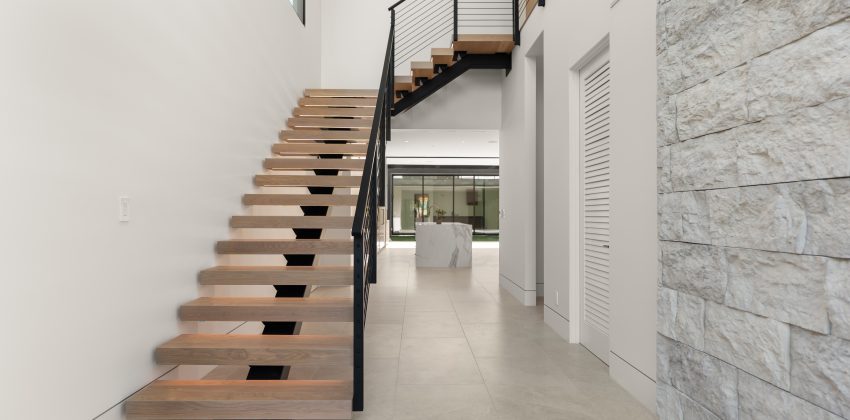 Modern floating wood staircase with black cable railing beside a stone accent wall in a Manhattan Beach custom home