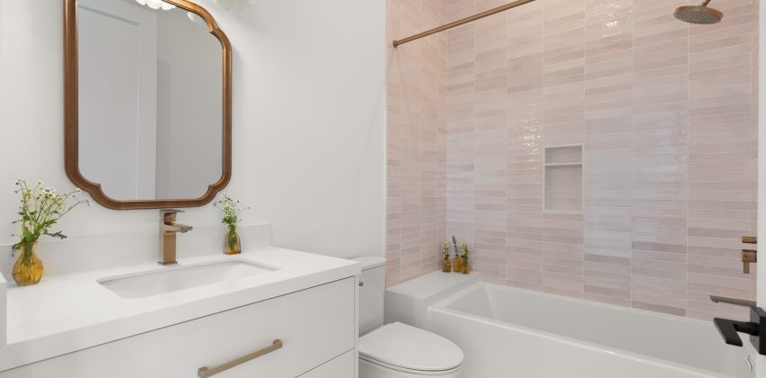 Bathroom with white floating vanity, brass fixtures and mirror, and pink tiled shower-tub combo in Manhattan Beach home
