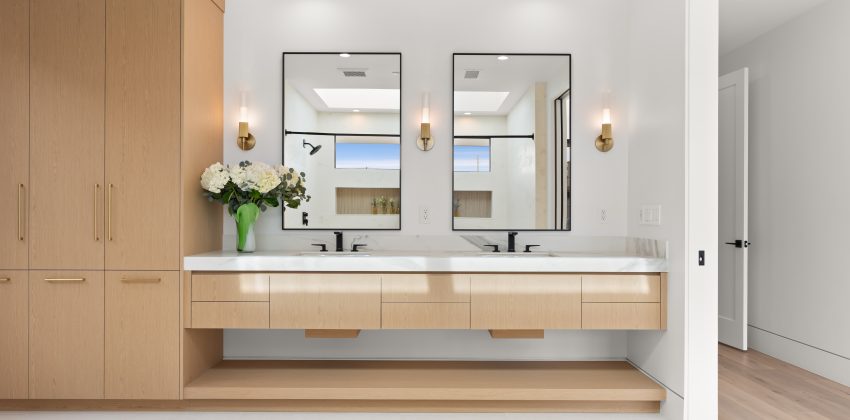 Primary bathroom with floating light wood double-sink vanity and floor-to-ceiling wardrobe cabinetry in Manhattan Beach home